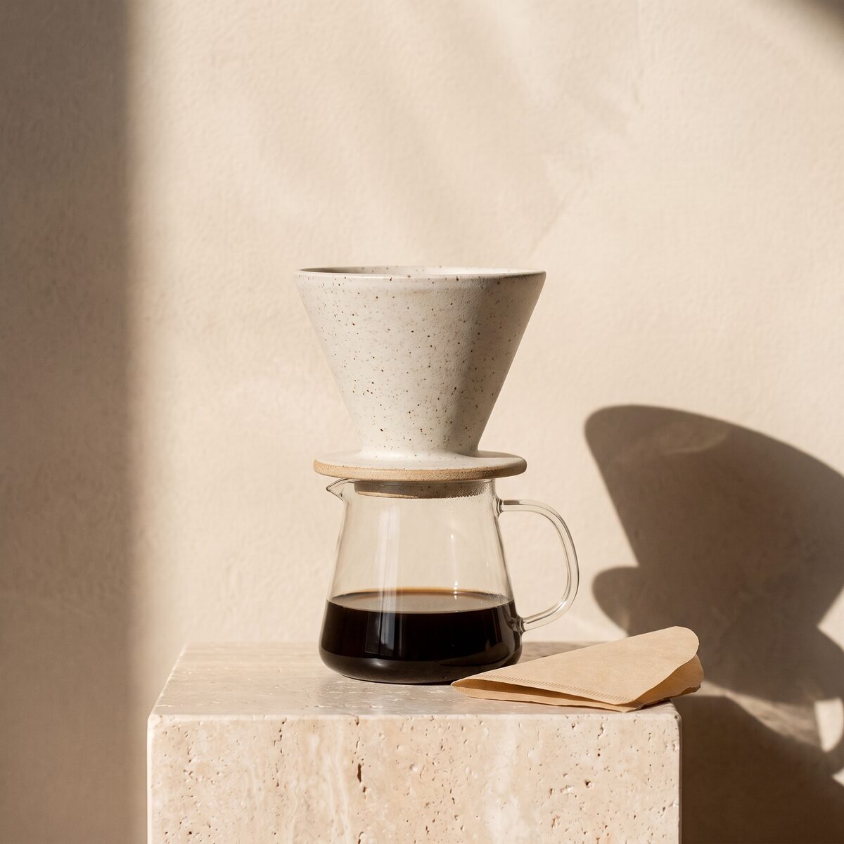 A speckled white stoneware pour-over dripper on a glass carafe of coffee, with a paper filter