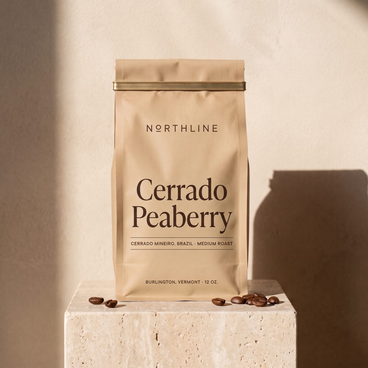 Cerrado Peaberry in a matte sand Northline coffee bag with a brass tie, on a travertine block against a plaster wall