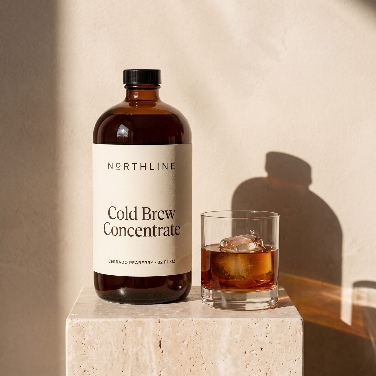 An amber glass bottle of Northline Cold Brew Concentrate beside a glass of cold brew over ice