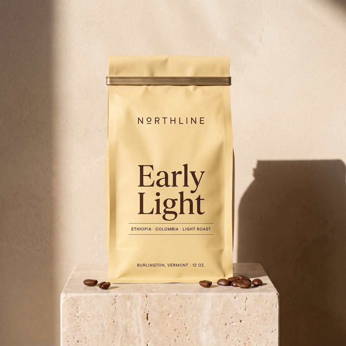 Early Light in a matte pale yellow Northline coffee bag with a brass tie, on a travertine block against a plaster wall