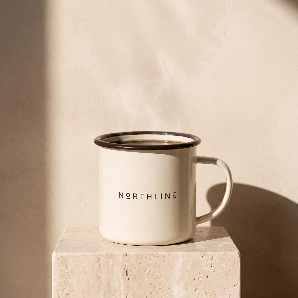 A cream enamel camp mug with a brown rim and the Northline wordmark, filled with black coffee