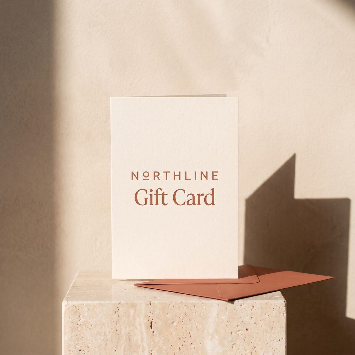A cream letterpress Northline gift card propped up beside a terracotta envelope