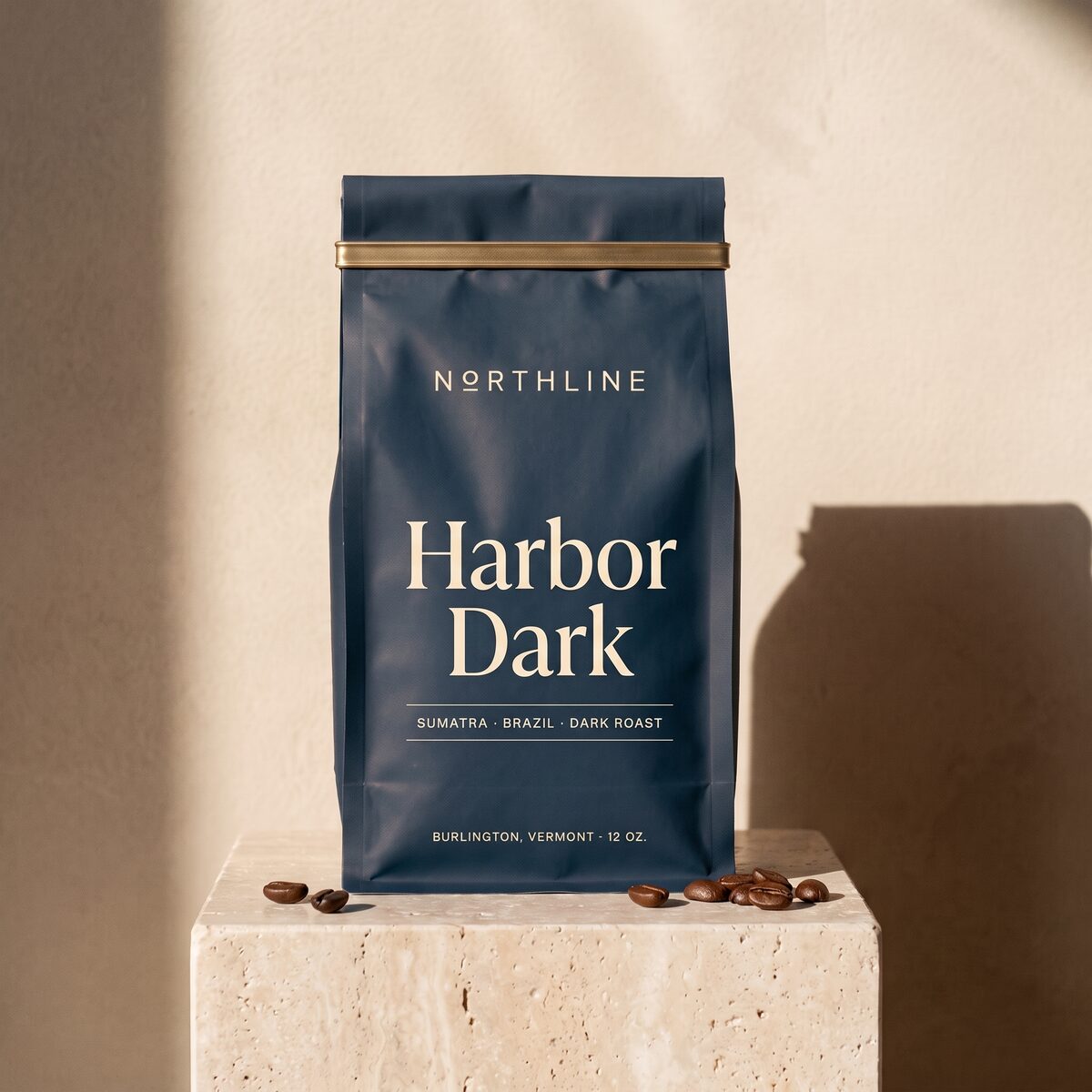 Harbor Dark in a matte navy Northline coffee bag with a brass tie, on a travertine block against a plaster wall