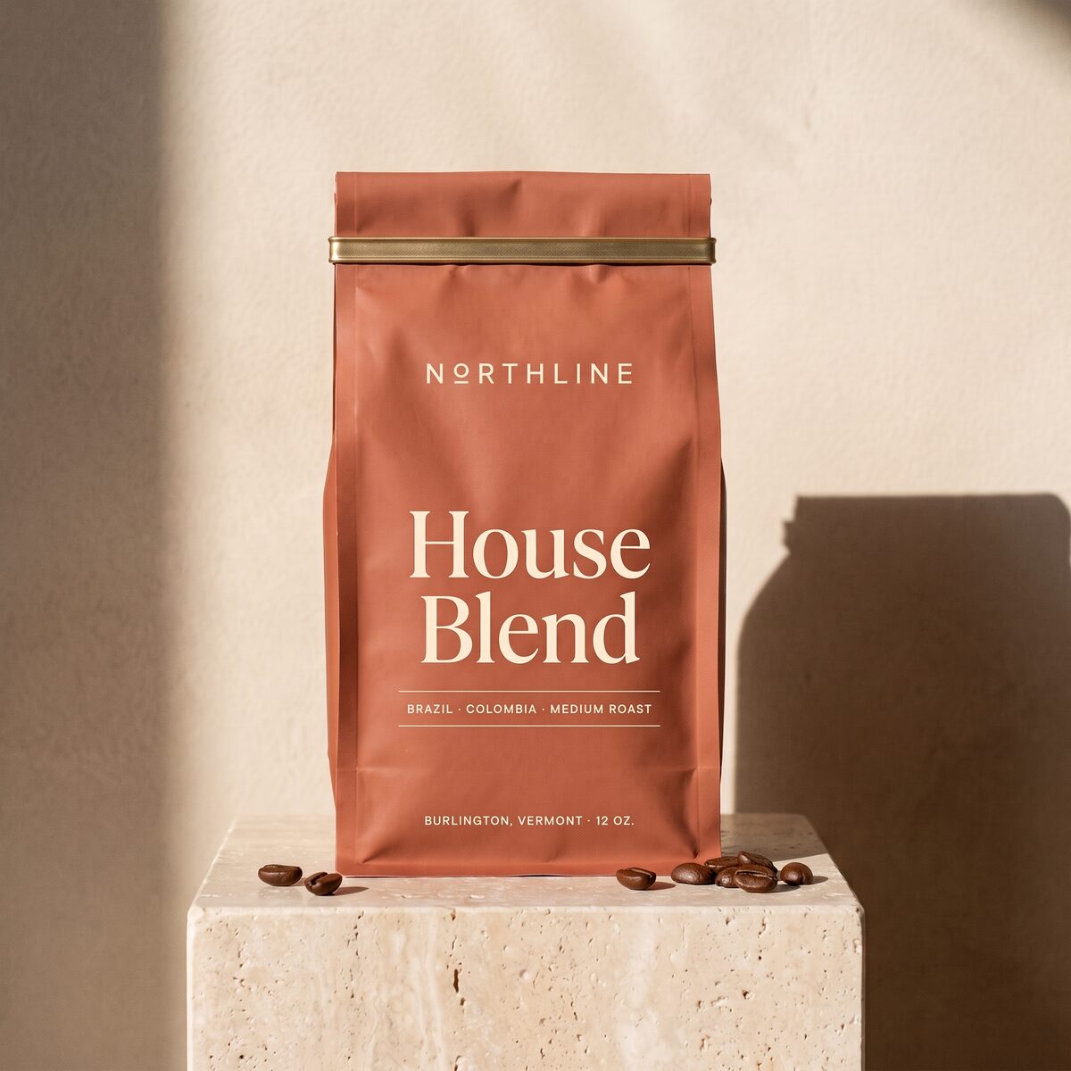 House Blend in a matte terracotta Northline coffee bag with a brass tie, on a travertine block against a plaster wall
