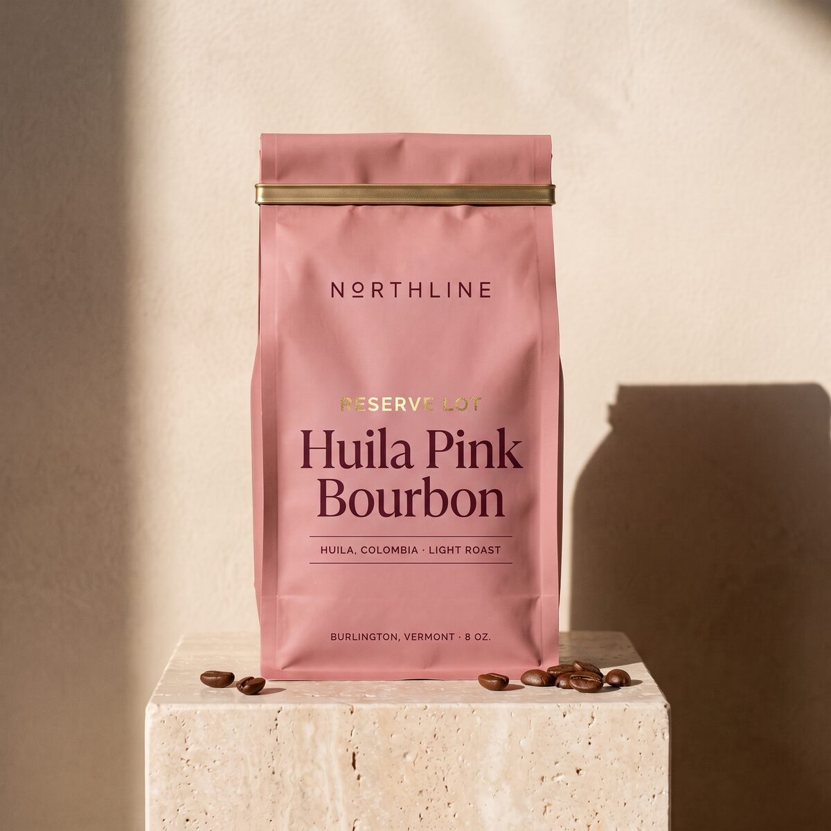 Huila Pink Bourbon, marked Reserve Lot, in a matte dusty rose Northline coffee bag with a brass tie, on a travertine block against a plaster wall