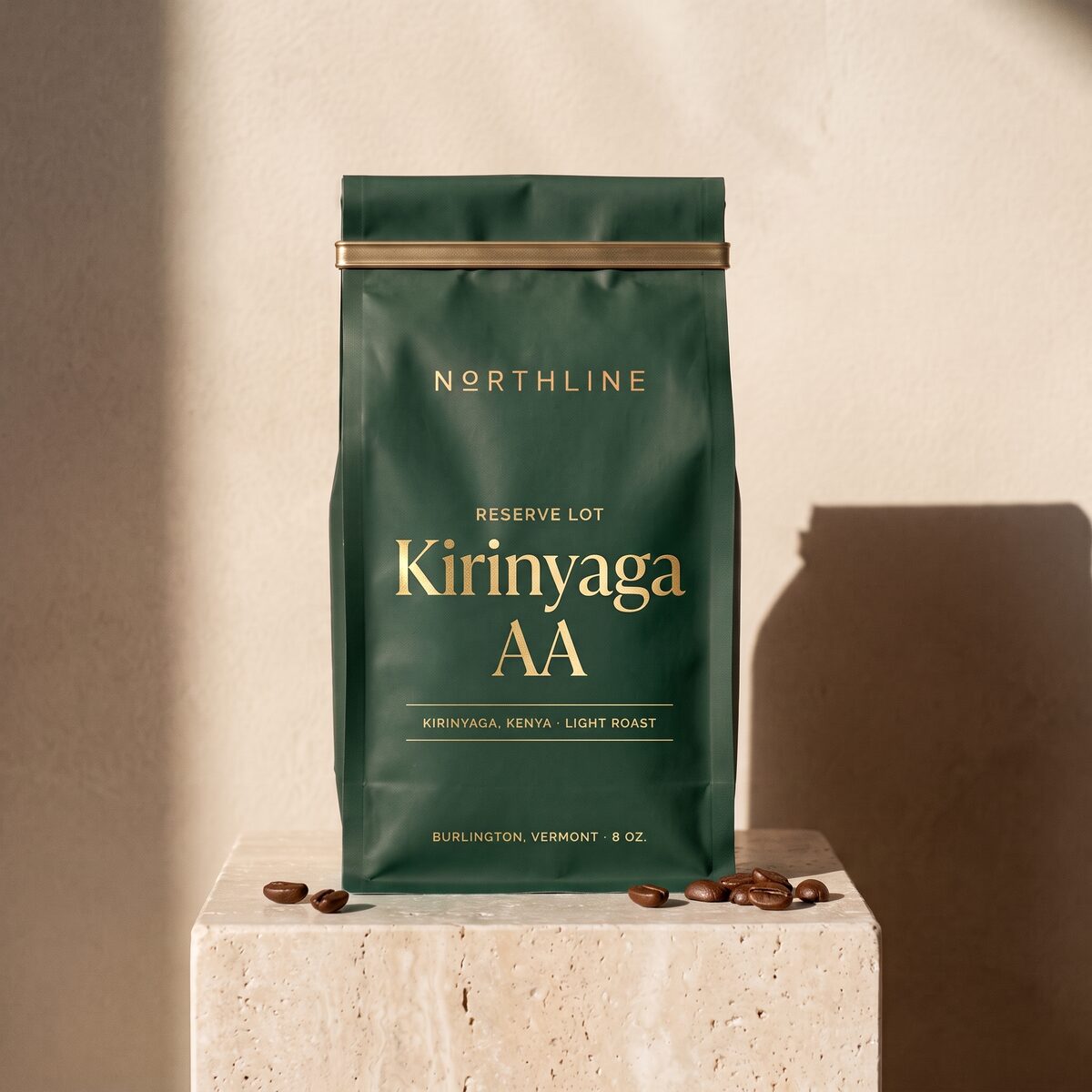 Kirinyaga AA, marked Reserve Lot in gold, in a matte bottle green Northline coffee bag with a brass tie, on a travertine block against a plaster wall