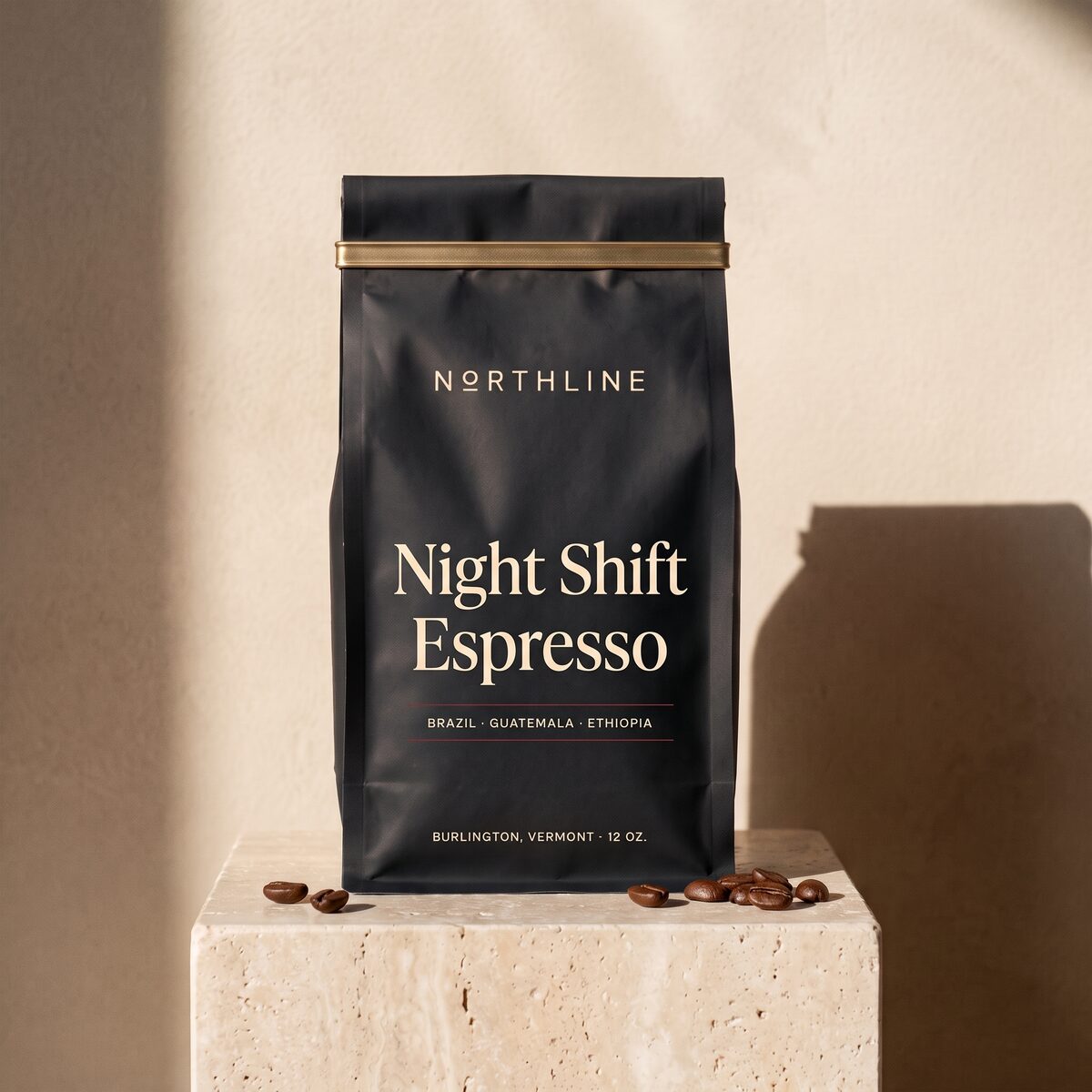 Night Shift Espresso in a matte black Northline coffee bag with a brass tie, on a travertine block against a plaster wall