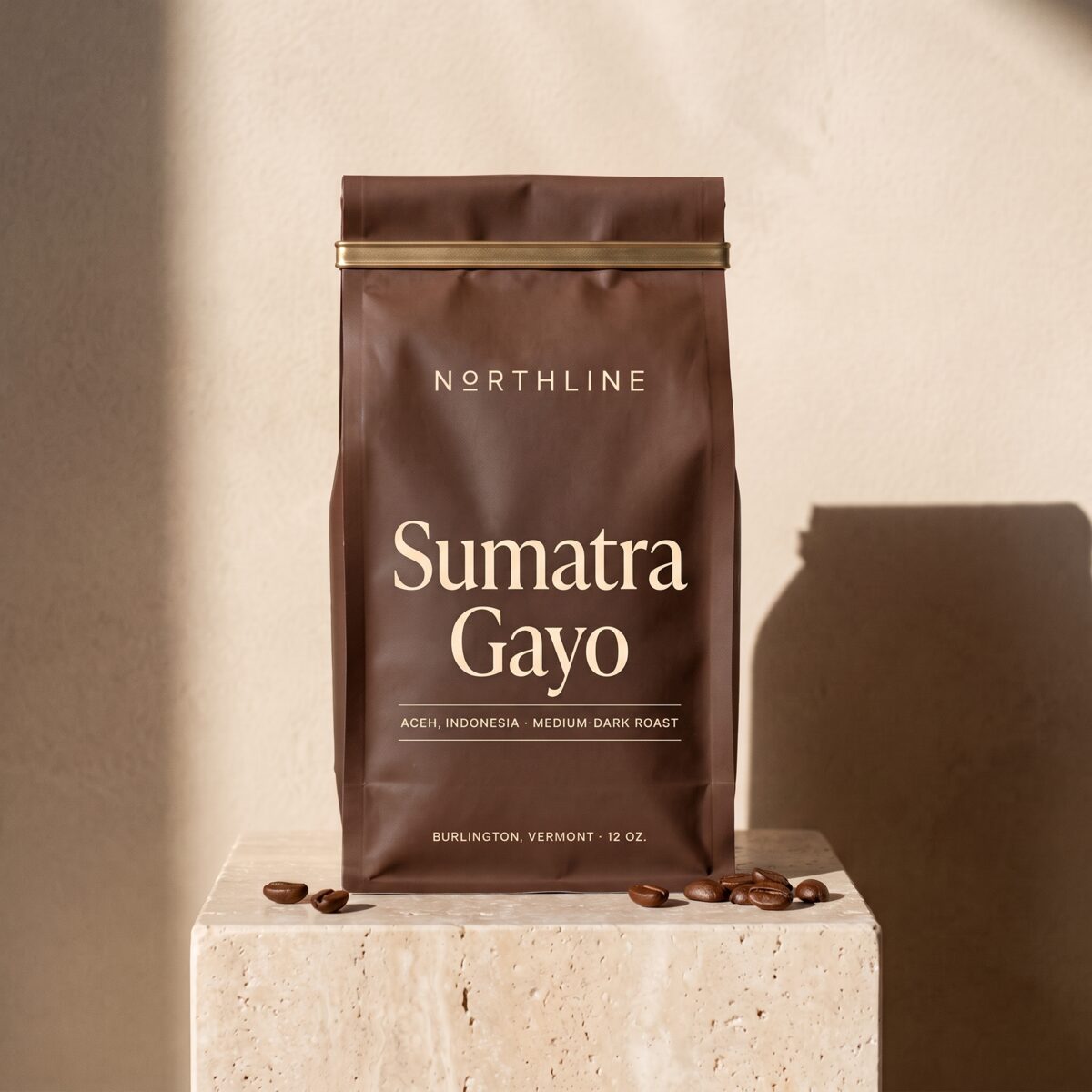 Sumatra Gayo in a matte chocolate brown Northline coffee bag with a brass tie, on a travertine block against a plaster wall
