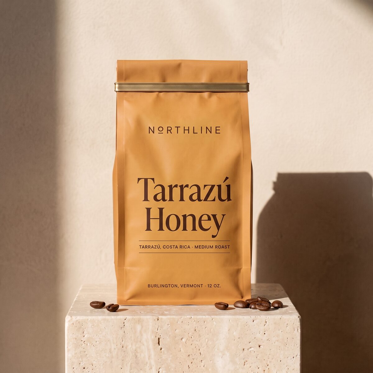 Tarrazú Honey in a matte honey ochre Northline coffee bag with a brass tie, on a travertine block against a plaster wall