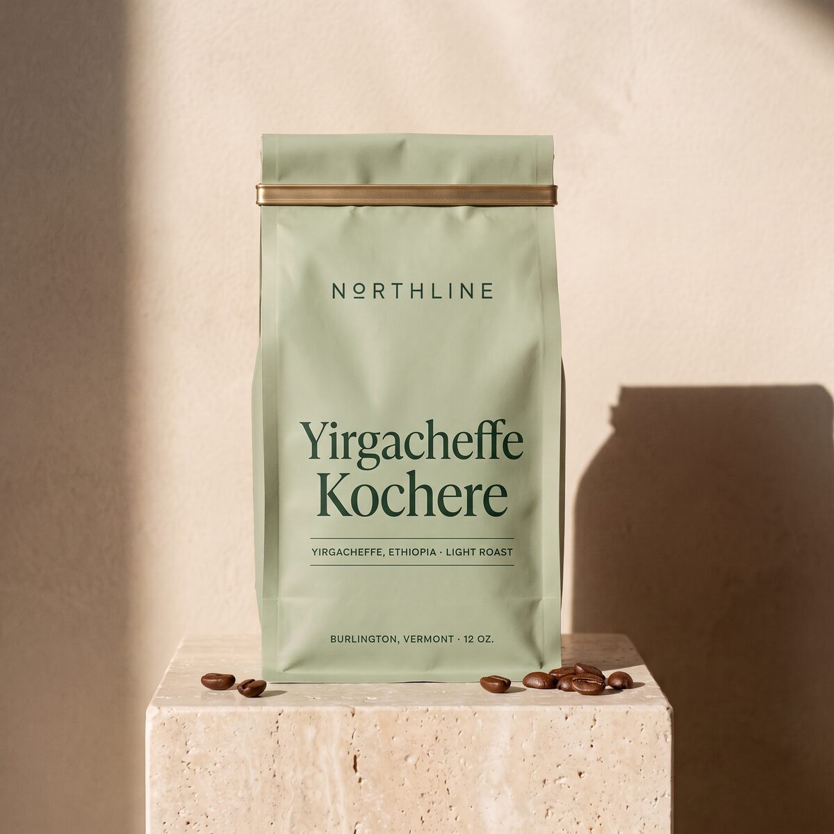 Yirgacheffe Kochere in a matte sage green Northline coffee bag with a brass tie, on a travertine block against a plaster wall